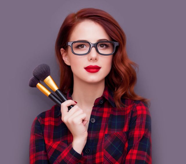 Young make-up artist with brushes on grey background